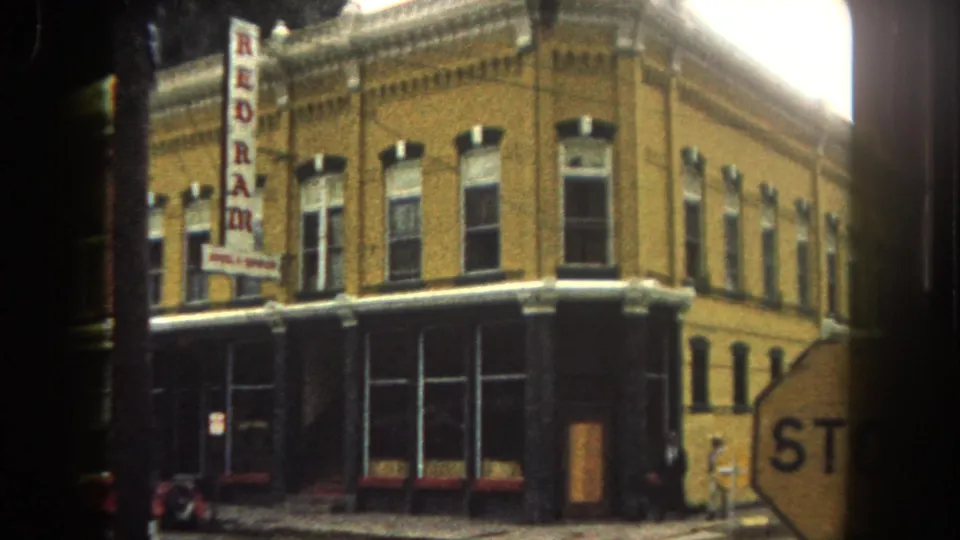 1962 Summit County commercial corner with yellow brick facade, storefront windows, vertical REDRAM sign, partial stop sign, and street edge.