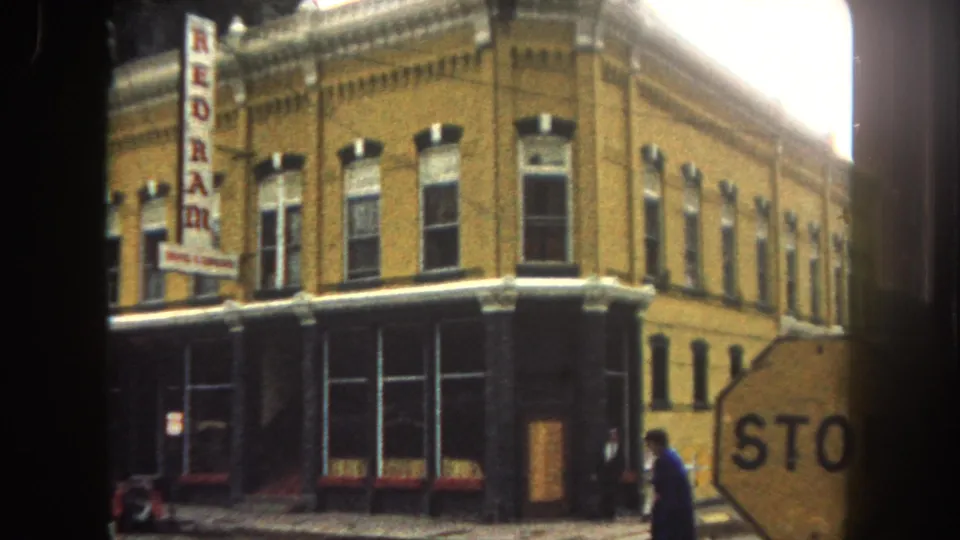 1962 Summit County street corner with yellow brick storefront, vertical REDRAM sign, partial stop sign, and an adult pedestrian at frame edge.