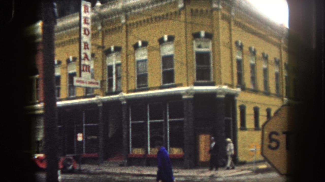 1962 Summit County corner storefront with REDRAM sign, partial stop sign in the foreground, pedestrians, and vehicles along the street.
