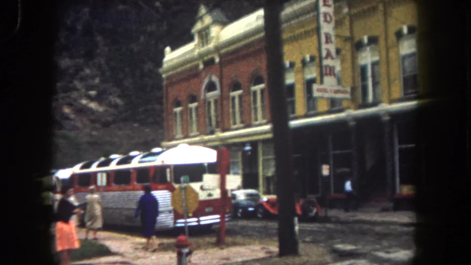 Summit County 1962 home-movie frame showing pedestrians near a classic bus outside a commercial building with a vertical REDRAM sign.