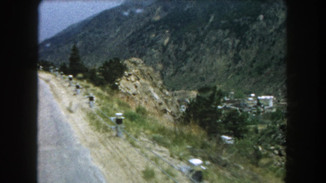 Summit County, Colorado road scene filmed on 8mm in 1962, showing a curving mountain road, white posts, and valley structures below.
