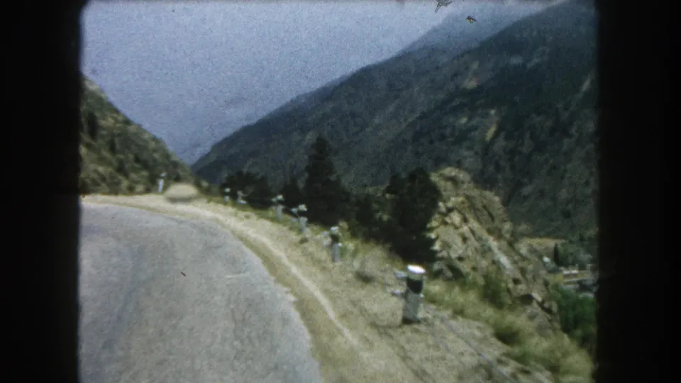 End frame of a 1962 Summit County, Colorado 8mm road view, with a curving mountain road, roadside posts, and forested slopes.