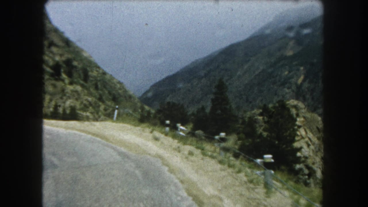 Moving 8mm view along a Summit County mountain road with green slopes and scattered pines.