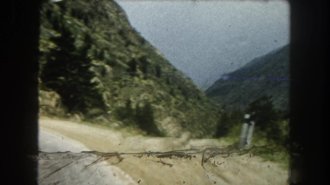 Winding mountain road seen through a vehicle window with trees and rocky slopes.
