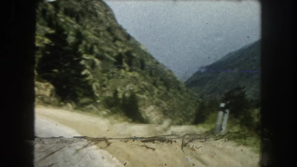 1962 Summit County road view from inside a vehicle, showing a winding mountain route, evergreen trees, and rocky slopes.