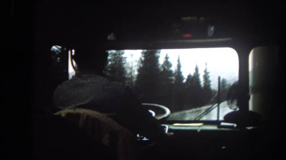 1962 bus interior in Summit County, with the driver at the wheel and a tree-lined mountain road visible through the windshield.