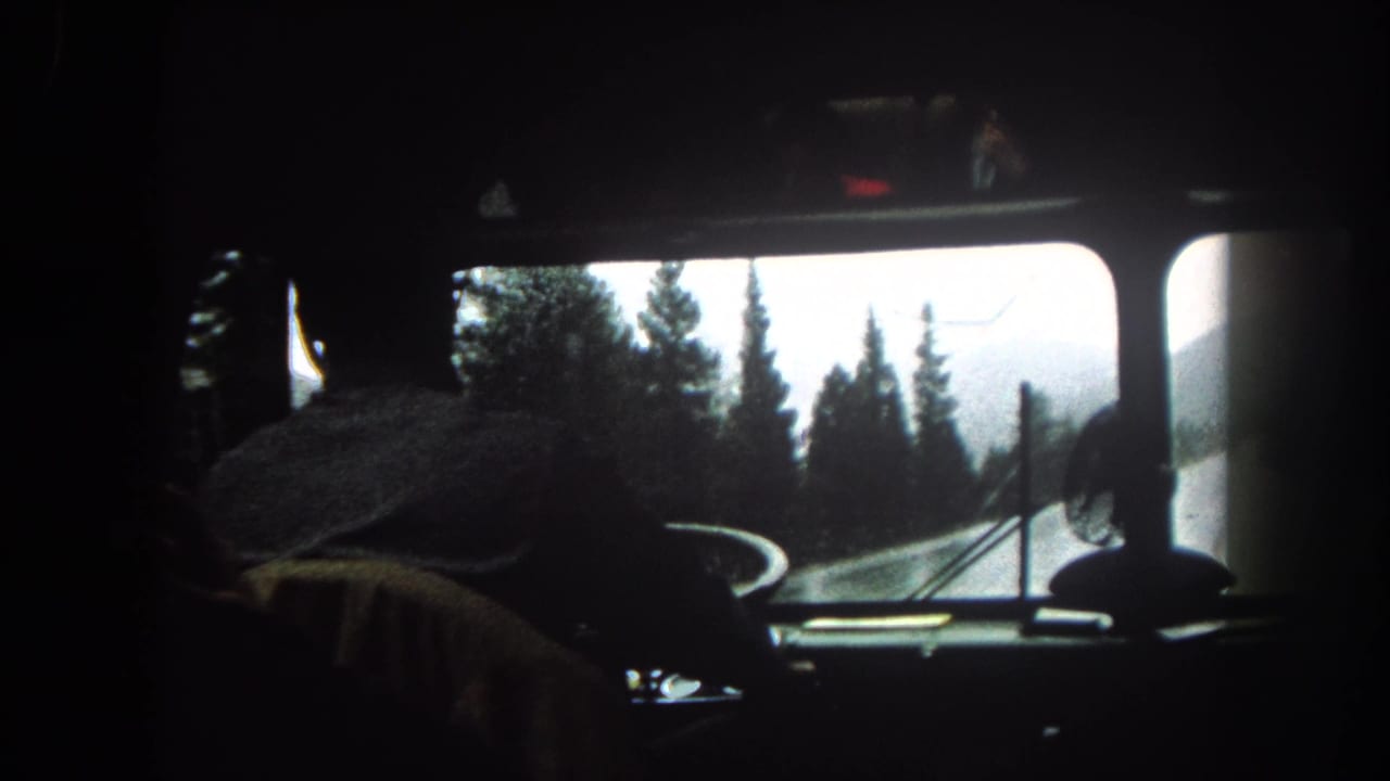 Interior 8mm view from a bus or large vehicle in Summit County, Colorado, with the driver silhouetted against a snowy pine road.