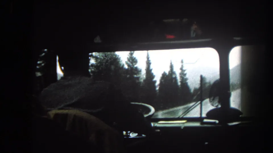 Interior 8mm view from a bus or large vehicle in Summit County, Colorado, with the driver silhouetted against a snowy pine road.