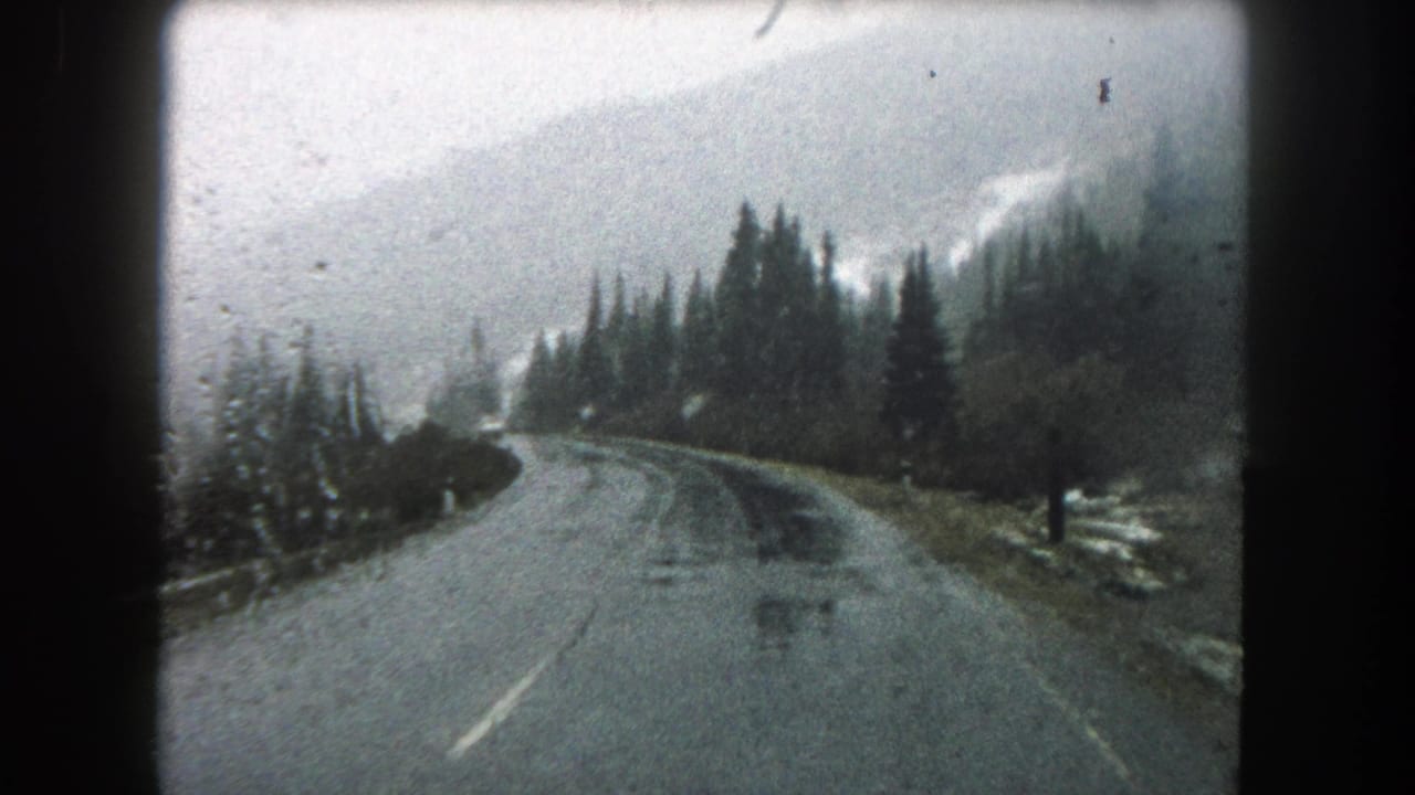 1962 8mm view from a moving vehicle on a wet, winding road through snowy evergreen terrain in Summit County, Colorado.