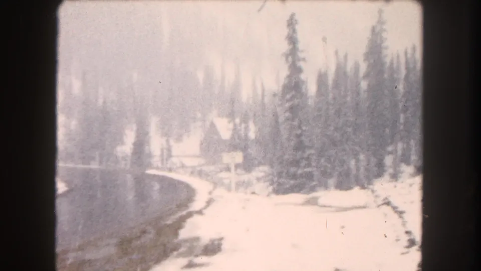 Final 8mm frame shows a snow-covered roadside in Summit County with a curved road, evergreens, and a lodge-like building softened by exposure and snowfall.