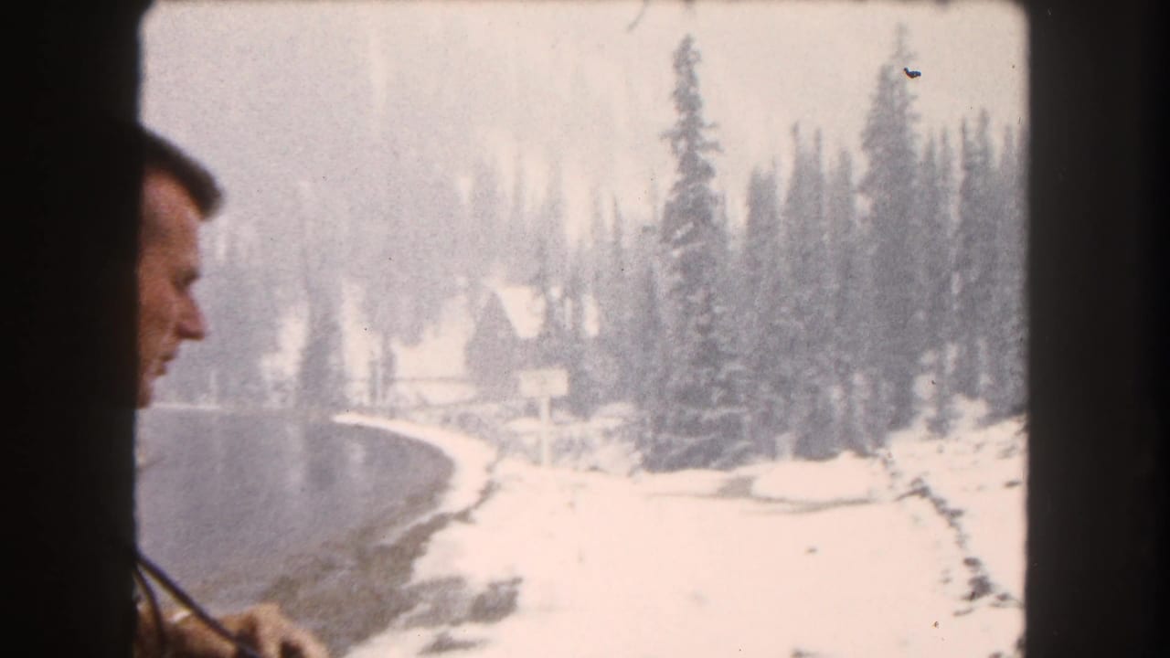 1962 Summit County, Colorado 8mm frame showing a partial adult man near a snowy lakeshore and evergreen forest.