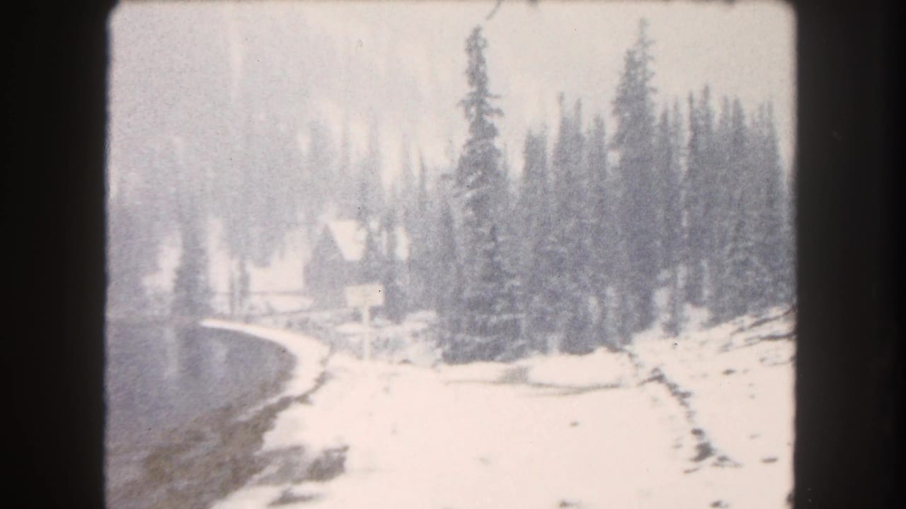 1962 Summit County, Colorado 8mm view of a snow-covered lakeshore with dense evergreens and muted winter light.
