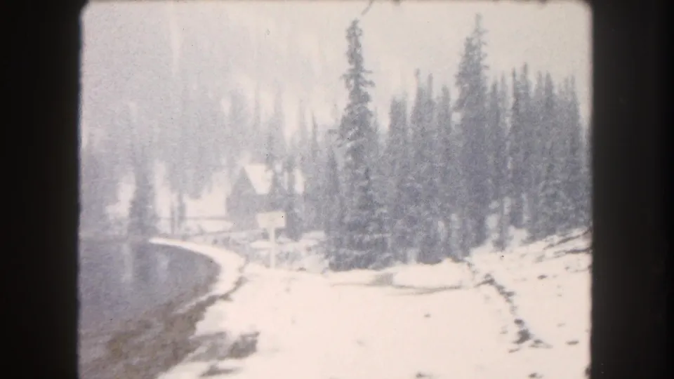 1962 Summit County, Colorado 8mm view of a snow-covered lakeshore with dense evergreens and muted winter light.