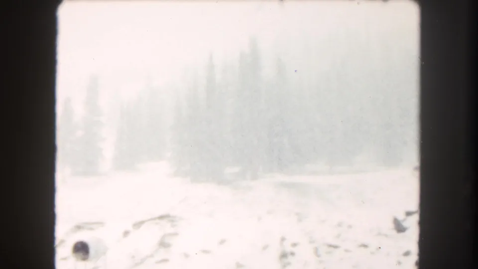 Overexposed 1962 Summit County, Colorado 8mm frame showing snow, faint evergreens, and a washed-out lakeshore area.