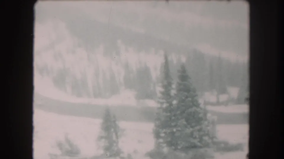 1962 Summit County 8mm frame with soft-focus snowfields, evergreen trees, and a curving road across the valley floor.