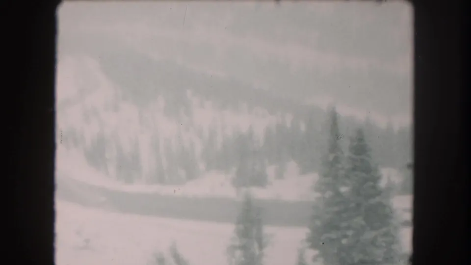 Faded-color 1962 8mm frame from Summit County, Colorado, showing a quiet snowy valley, evergreens, and a winding road.