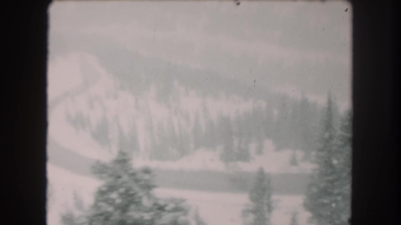 1962 Summit County, Colorado 8mm frame showing a snow-covered slope, evergreen trees, and a winding road in soft focus.