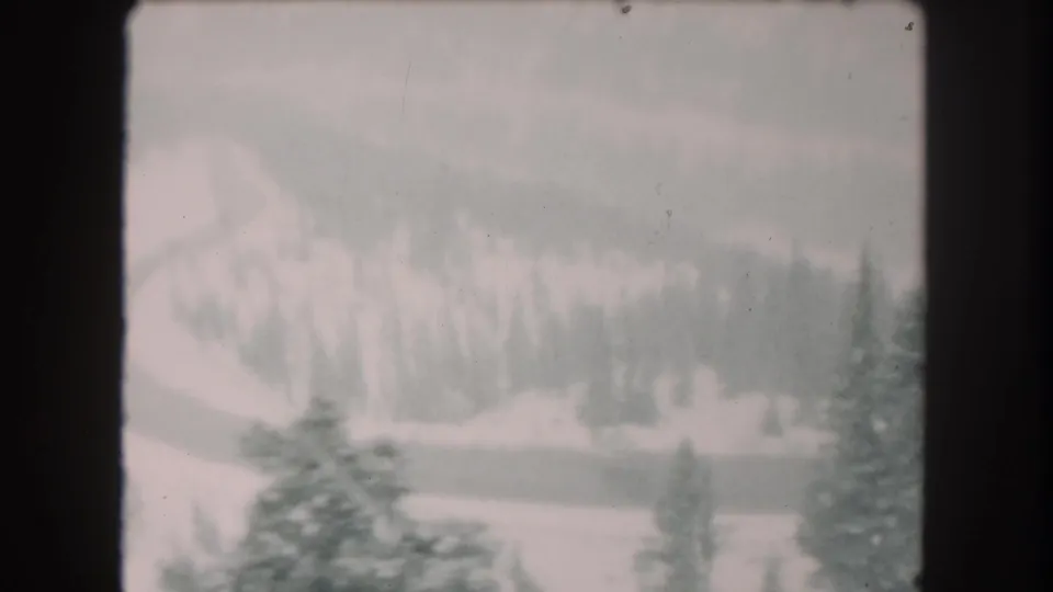 1962 Summit County, Colorado 8mm frame showing a snow-covered slope, evergreen trees, and a winding road in soft focus.