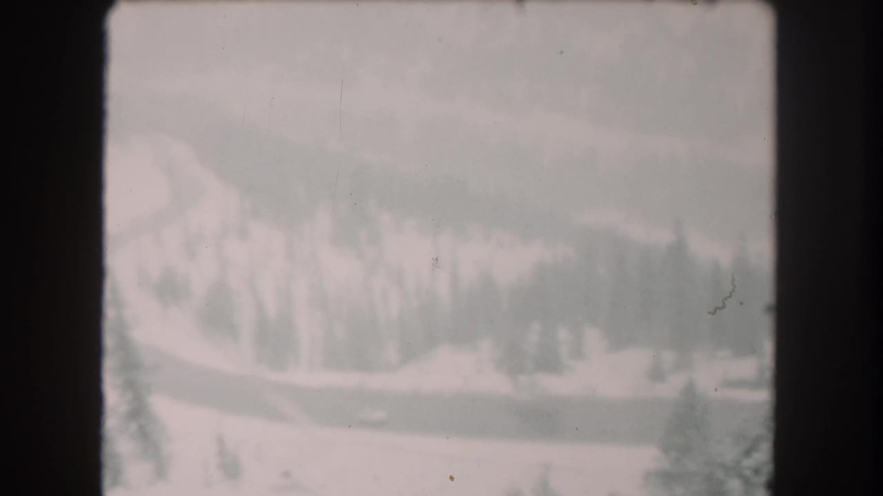 1962 Summit County, Colorado 8mm frame with a winding snowbound highway, evergreen trees, and a distant vehicle.
