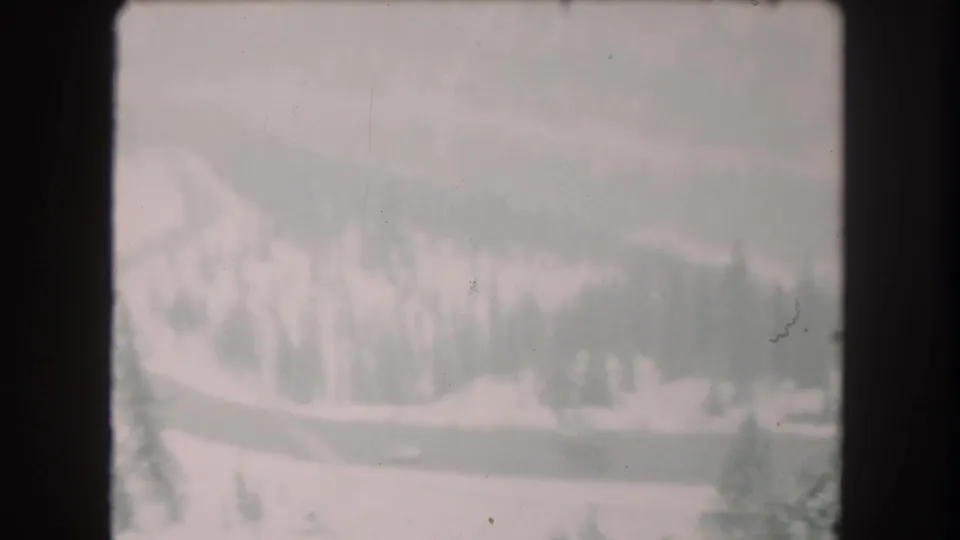 1962 Summit County, Colorado 8mm frame with a winding snowbound highway, evergreen trees, and a distant vehicle.