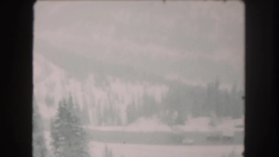 1962 Summit County, Colorado frame showing a snow-edged road, evergreen trees, and faint distant traffic on 8mm film.