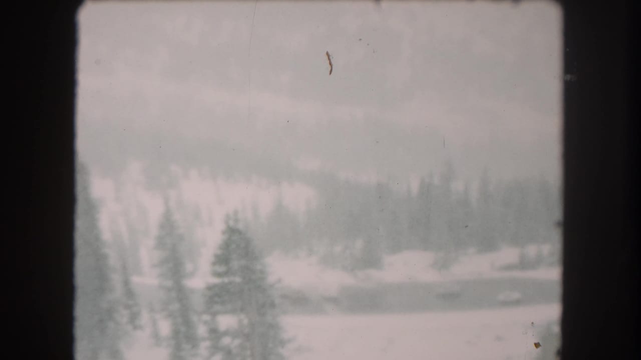 1962 Summit County, Colorado winter view with snow, evergreen forest, distant slope, and visible small-gauge film borders.