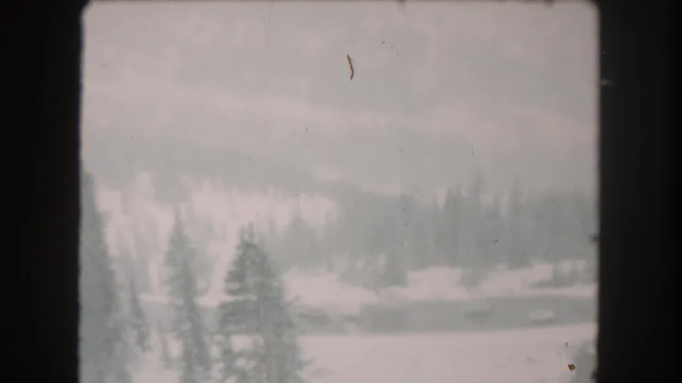 1962 Summit County, Colorado winter view with snow, evergreen forest, distant slope, and visible small-gauge film borders.