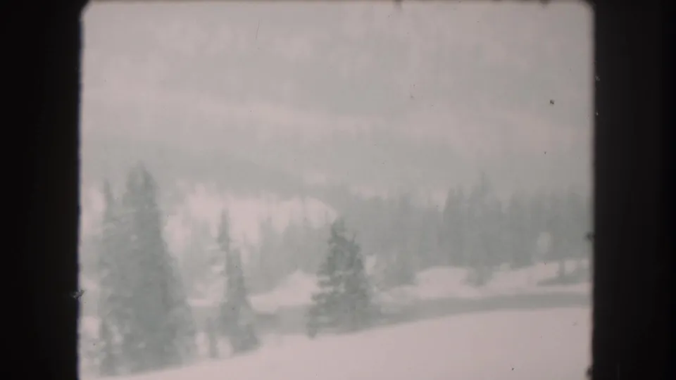 1962 Summit County, Colorado home-movie frame showing a snow-covered hillside, scattered pines, and a muted mountain backdrop.