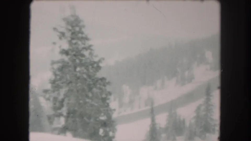 1962 Summit County, Colorado 8mm frame with a prominent evergreen, snow-covered slope, and distant forested mountain terrain.