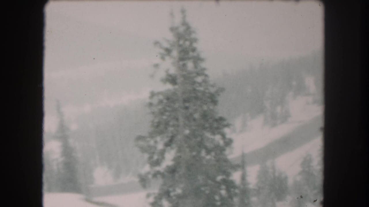 1962 Summit County, Colorado home-movie frame showing a snow-covered evergreen landscape and distant wooded hills in soft focus.