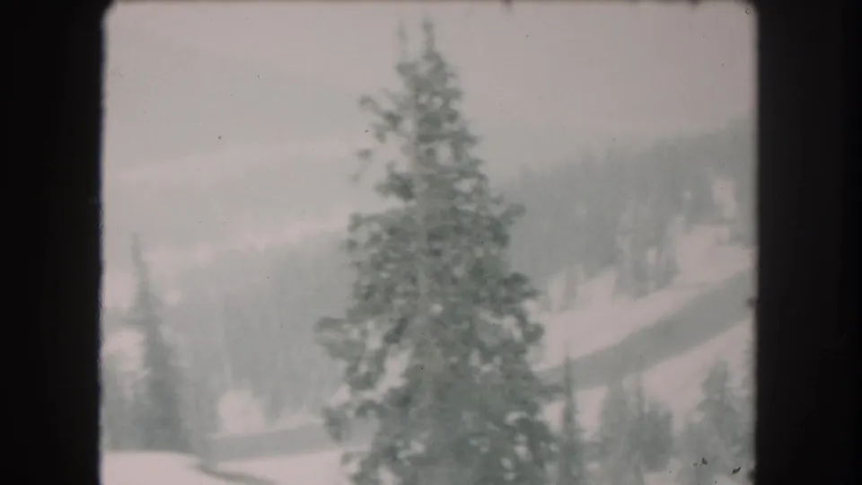 1962 Summit County, Colorado home-movie frame showing a snow-covered evergreen landscape and distant wooded hills in soft focus.