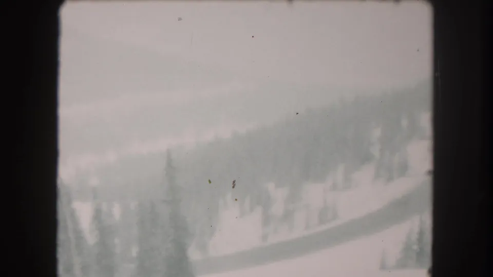 1962 Colorado home-movie frame with hazy snow-covered terrain, evergreen trees, and distant wooded slopes.