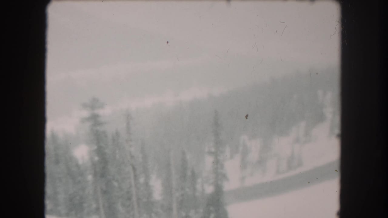 Snowy forested mountain slope seen through soft haze and dark 8mm frame borders.