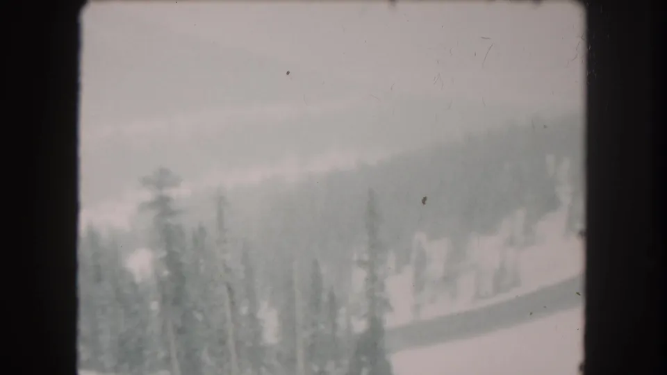1962 Summit County, Colorado 8mm frame showing a low-visibility snowy forest slope with muted ridges in the distance.