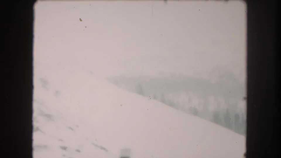1962 Summit County, Colorado frame showing an open snow-covered slope and faint treeline under washed-out winter haze.