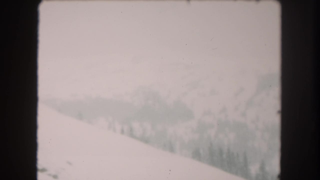 1962 8mm home-movie view of snowy Summit County mountain terrain with a pale slope, distant trees, and hazy sky.