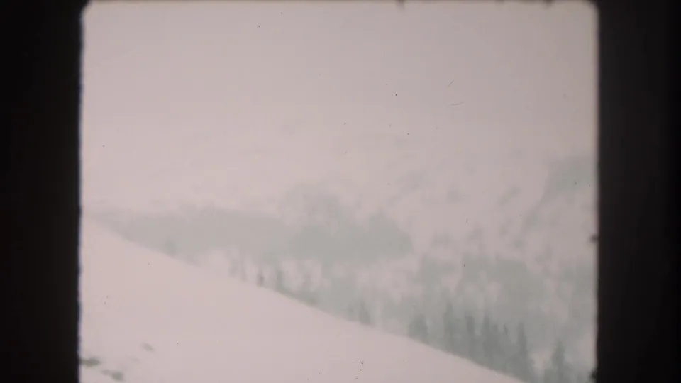 1962 8mm home-movie view of snowy Summit County mountain terrain with a pale slope, distant trees, and hazy sky.