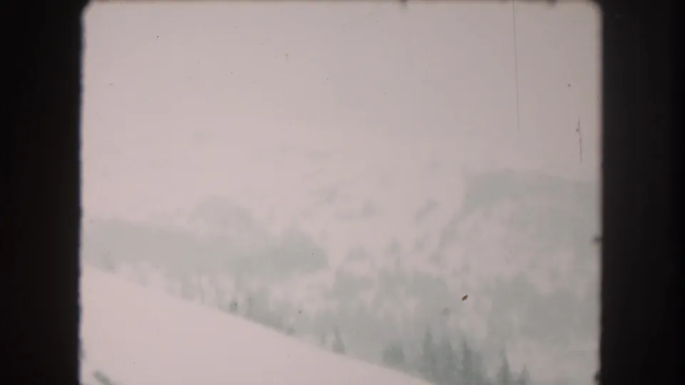 Soft 8mm frame of Summit County snow terrain with a bright valley floor and faint wooded slope in the distance.