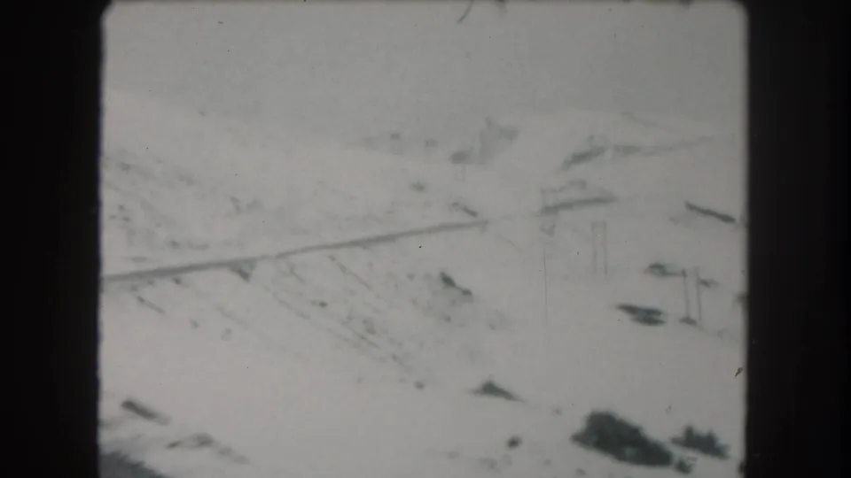 1962 8mm view of Summit County snowy terrain, with gullied slopes, dark exposed patches, and a faint line across the valley.