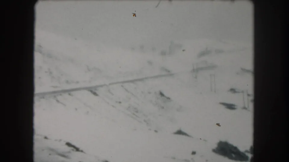 1962 Summit County, Colorado home-movie frame showing a snowy mountain road, faint utility poles, and soft 8mm edges.
