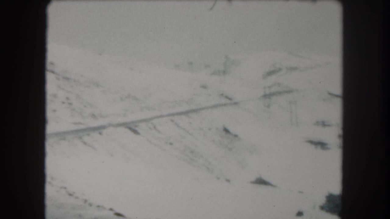Snowy roadside slope with a diagonal road and utility poles in the distance.