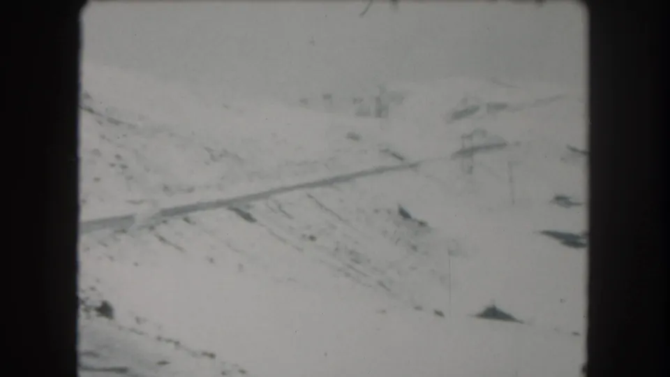 1962 Summit County, Colorado 8mm frame showing a snowy road scene with faint poles and low-contrast mountain terrain.