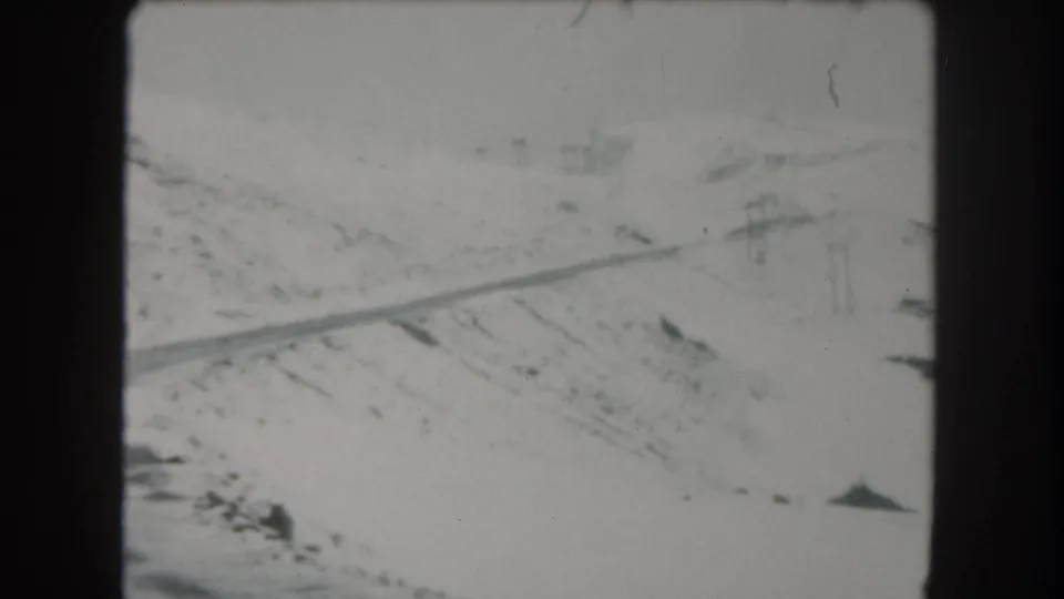 1962 Summit County, Colorado frame of a snowbound road across a hillside, with utility poles and scattered dark roadside shapes.