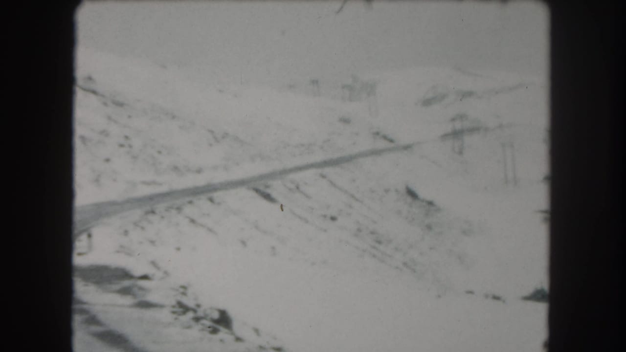 1962 8mm frame of a snow-covered road crossing a mountain landscape in Summit County, Colorado.