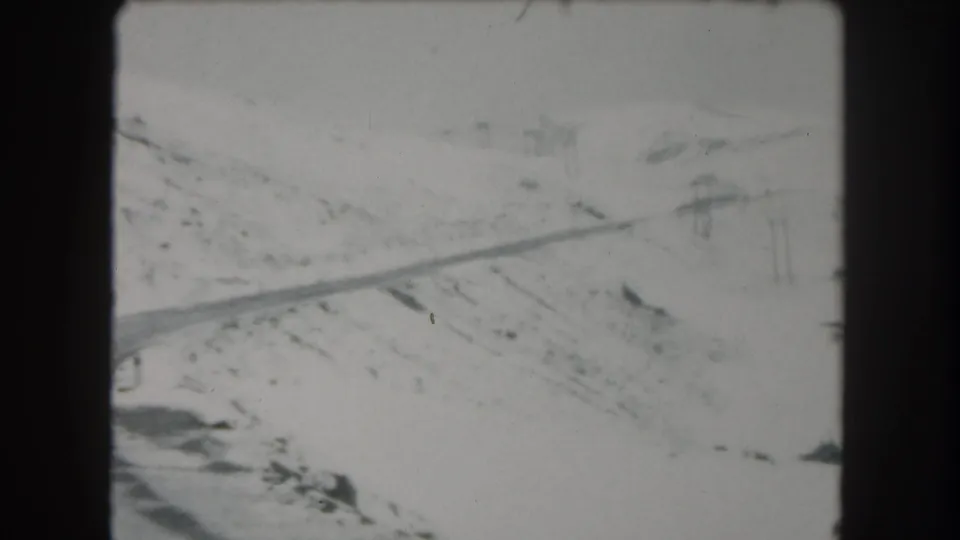 1962 8mm frame of a snow-covered road crossing a mountain landscape in Summit County, Colorado.