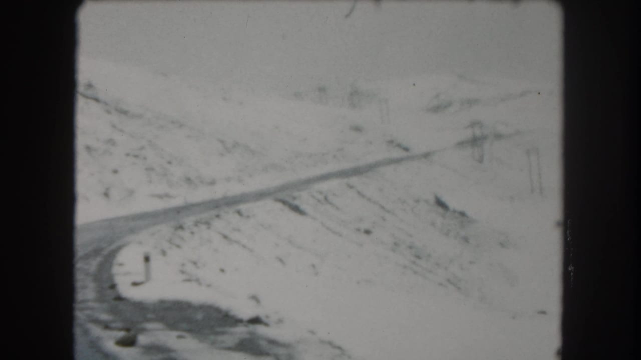 A snowy Summit County road curves through a sparse mountain landscape in a soft 8mm frame.