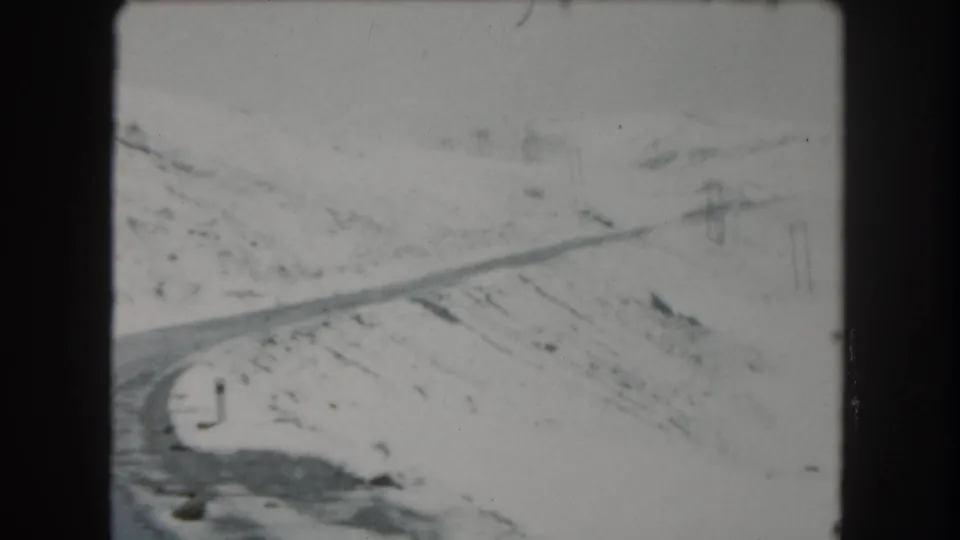 A snowy Summit County road curves through a sparse mountain landscape in a soft 8mm frame.