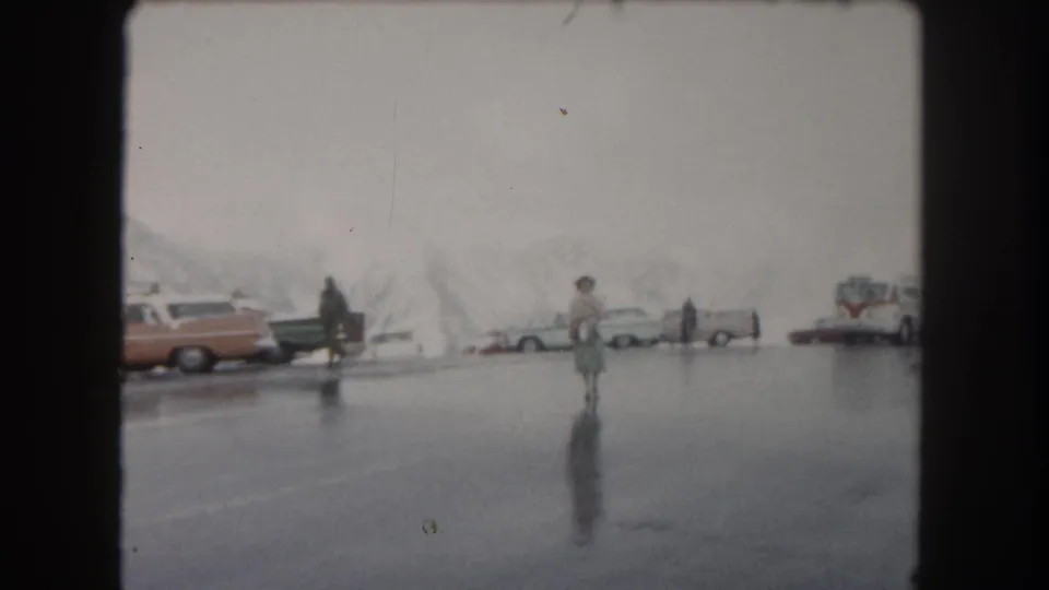 1962 8mm view of a wet Summit County parking area with parked classic cars and pedestrians.