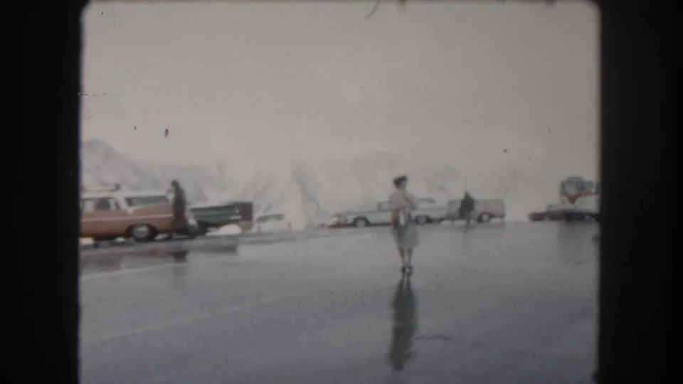 A woman in light clothing crosses a wet parking area near classic cars in Summit County, Colorado.