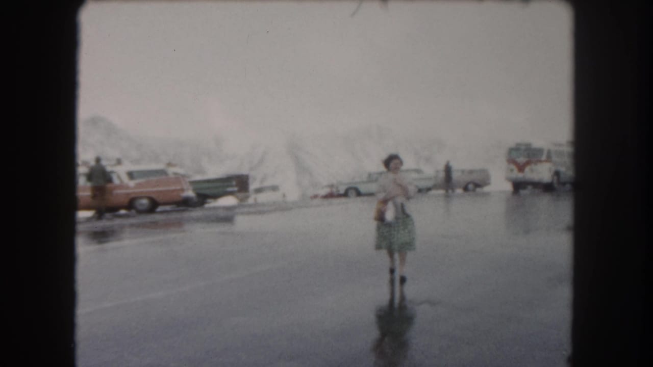 The woman moves closer through the Summit County parking lot, carrying a bag as cars, a bus, and icy snowbanks sit behind her.